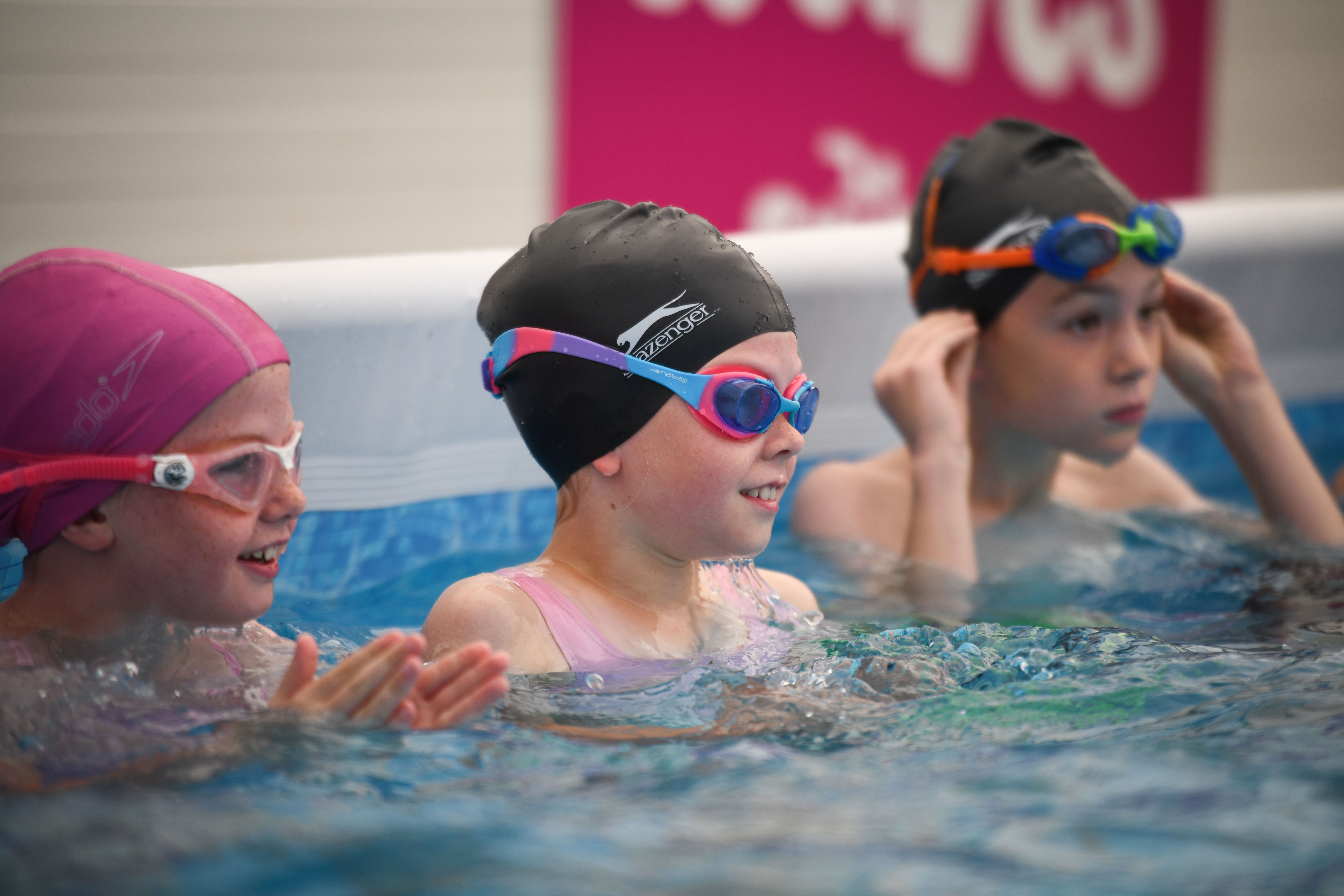 three children in the pool listening to a swim instructor - part of their swimming education